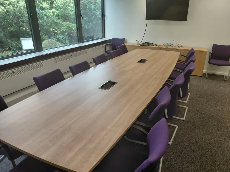 Long office meeting table with purple chairs and a wall-mounted screen