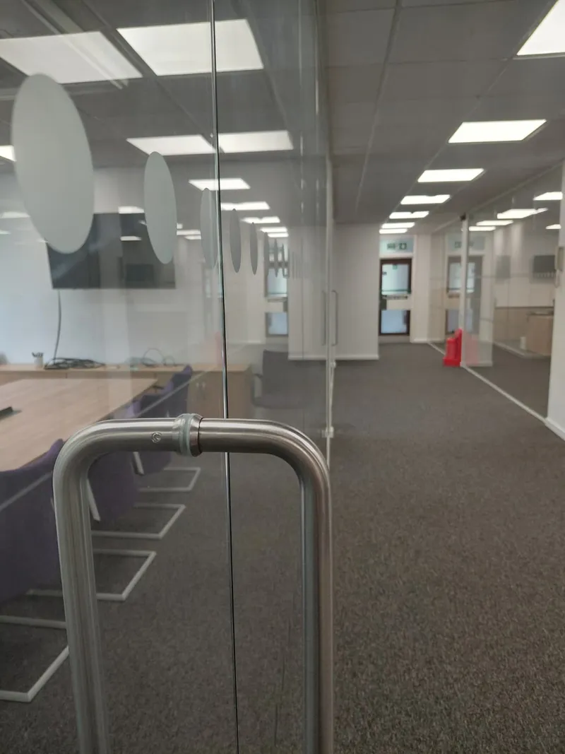 Office meeting room glass door with metal handle beside a carpeted corridor