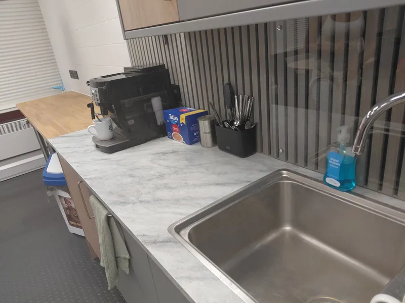 Office kitchen worktop beside a stainless steel sink and coffee machine