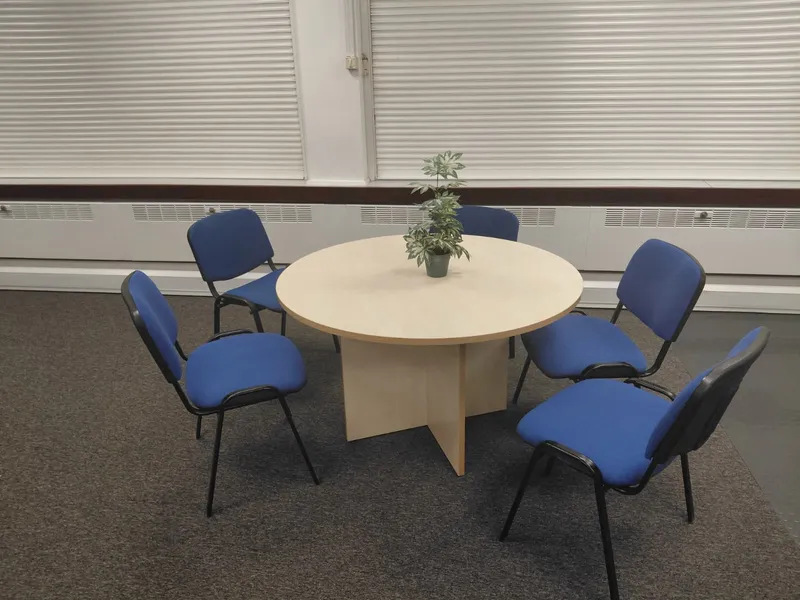Round meeting table with five blue chairs on an office carpet